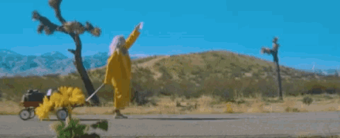a woman in a yellow dress is pushing a red wagon .