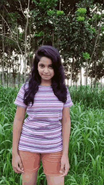 a girl in a striped shirt and shorts is standing in a field of tall grass .