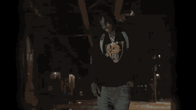 a young man with dreadlocks and a backpack is standing in front of a wall with graffiti on it .