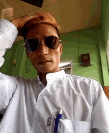a man wearing sunglasses and a hat holds his hand to his head