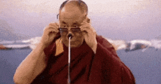 a man in a red robe is adjusting his glasses while holding a microphone in his mouth .