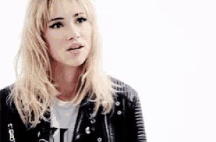 a blonde woman wearing a black leather jacket and a white t-shirt is standing in front of a white background .
