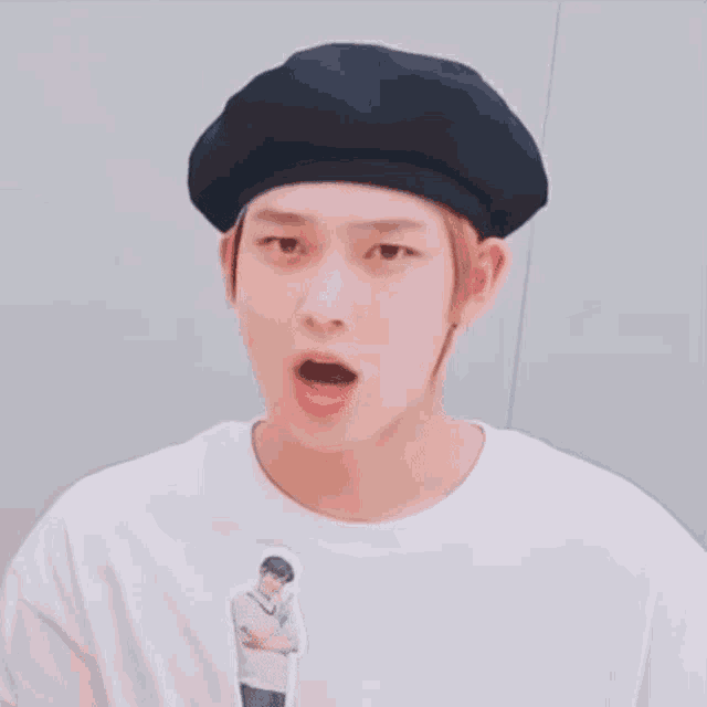 a young man wearing a black beret and a white t-shirt is holding a puppet of himself .