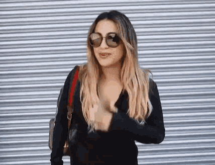 a woman wearing sunglasses is standing in front of a metal shutter .