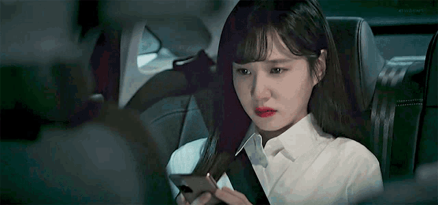 a woman in a white shirt is sitting in the back seat of a car looking at her phone .