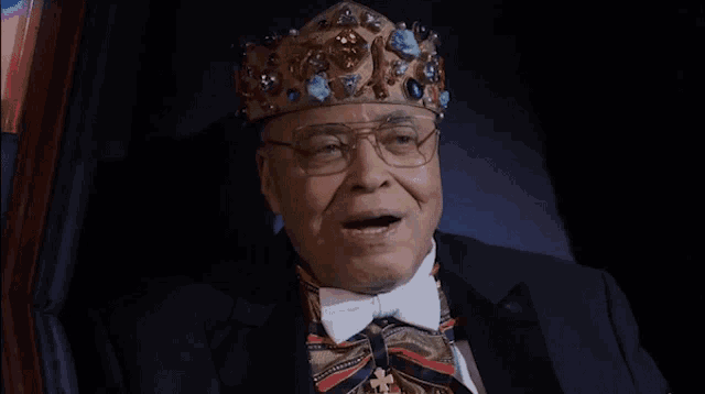a man wearing a crown and a bow tie is sitting in a chair
