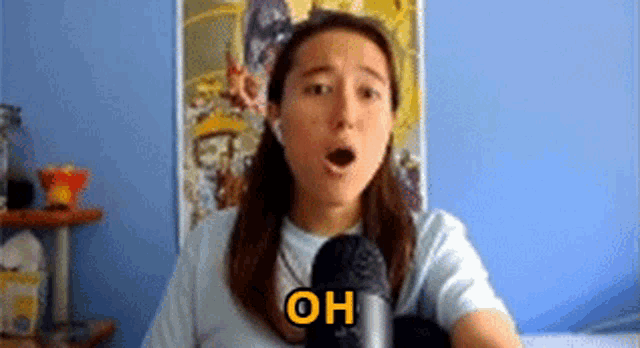 a woman is talking into a microphone with her mouth open and the word oh is on the screen .