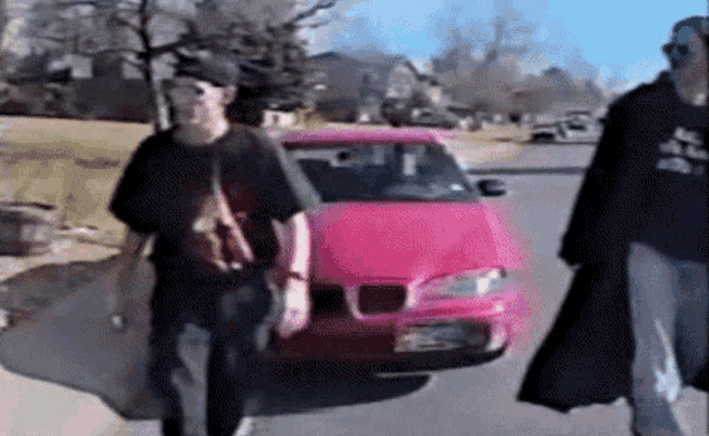 two men are walking down a street next to a pink bmw car