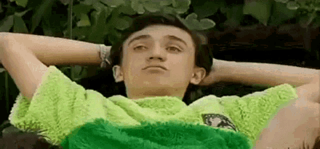 a young man is laying down with his hands behind his head .