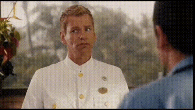a man in a white uniform with gold buttons is talking to another man in a blue shirt