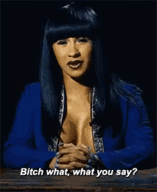 a woman in a blue jacket is sitting at a table with her hands folded and says bitch what what you say ?