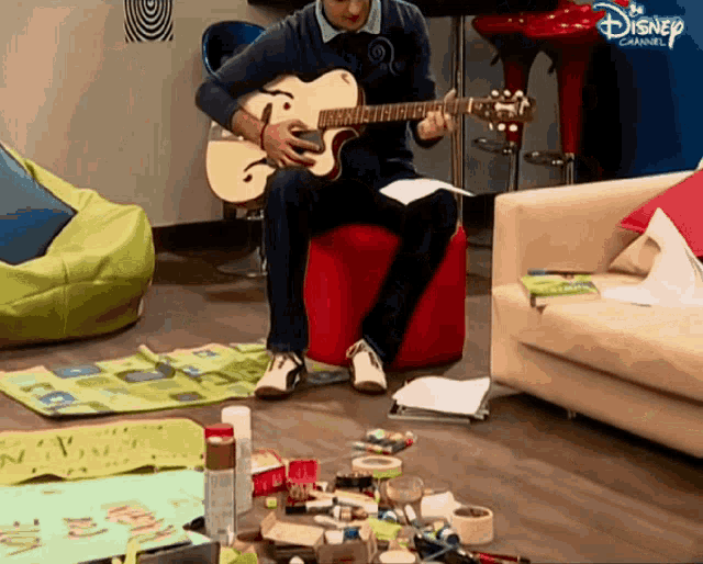 a man sits on an ottoman playing a guitar with a disney channel logo above him