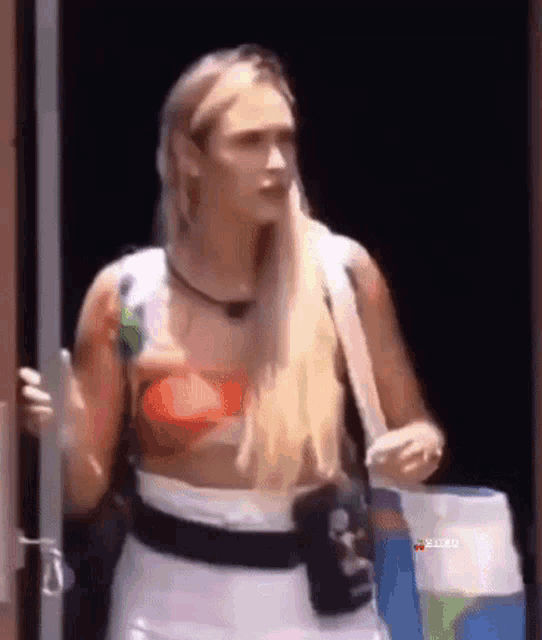 a woman with long blonde hair is standing in a doorway holding a bottle of soda .
