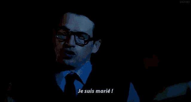 a man with glasses says je suis marie in a dark room