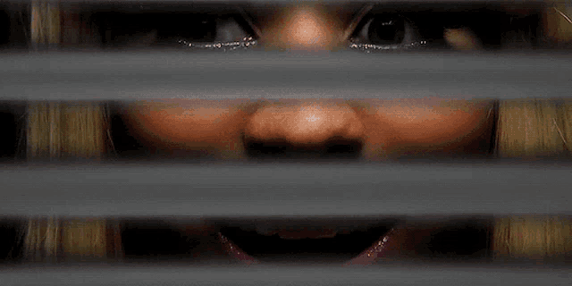 a close up of a woman 's face looking through blinds