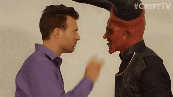 a man in a purple shirt is standing next to a man in a red demon mask .