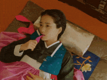 a woman in a traditional korean dress is laying on a bed with a pink blanket