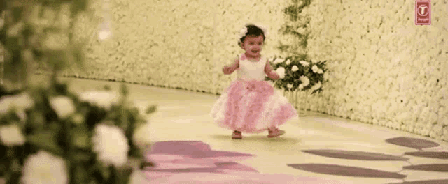 a little girl in a pink and white dress is walking on a floral floor .