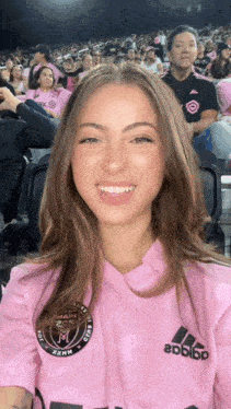 a woman wearing a pink adidas shirt smiles in front of a crowd