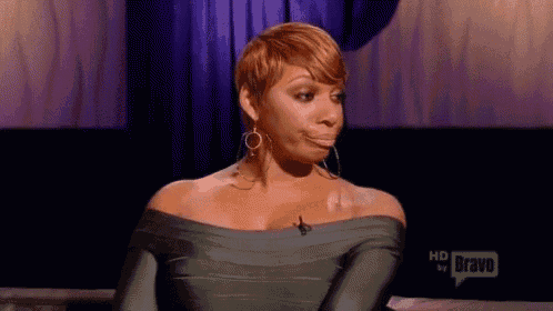 a woman is making a funny face while sitting on a couch in front of a purple curtain .