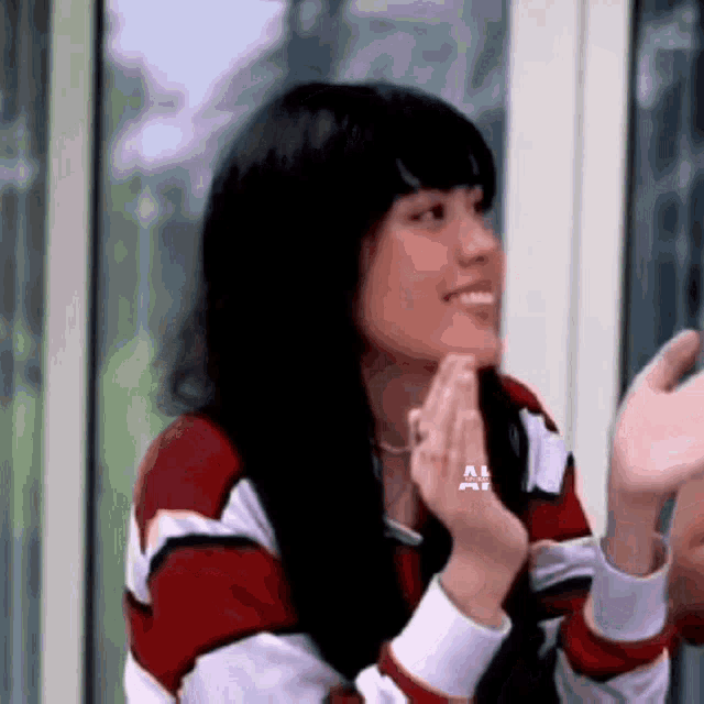 a woman wearing a red and white striped sweater is smiling and clapping her hands