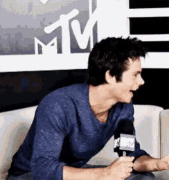a man is sitting on a couch holding a microphone with a mtv logo behind him