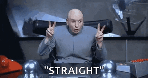 dr. evil is sitting at a desk and giving a peace sign .