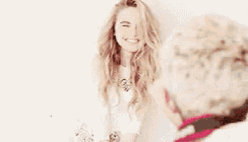 a young woman in a white dress is smiling while standing in front of a white wall .