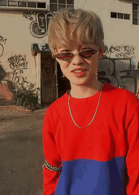 a boy wearing sunglasses stands in front of a wall with graffiti on it that says " stupid crime "