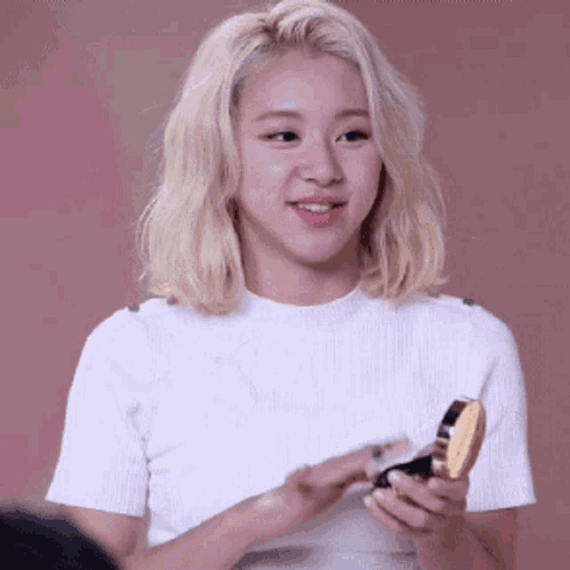 a blonde woman in a white shirt is holding a compact mirror .