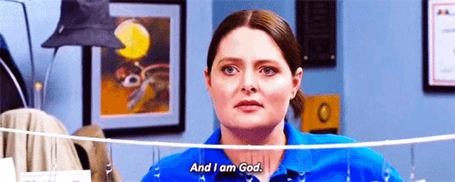 a woman in a blue shirt is standing in front of a rope and says `` and i am god . ''