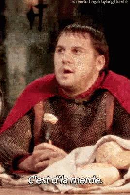 a man in a red cape is sitting at a table with bread and says c'est d'la merde