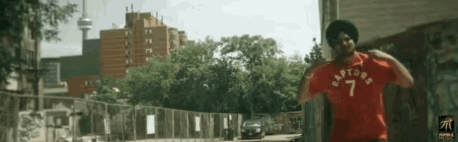 a man wearing a red raptors shirt is walking down a street