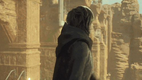 a man in a black hooded jacket stands in front of a building