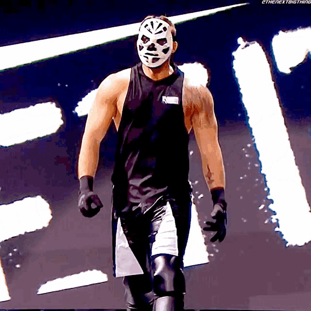 a man wearing a mask and a black tank top stands in front of a sign that says ' the next thing '