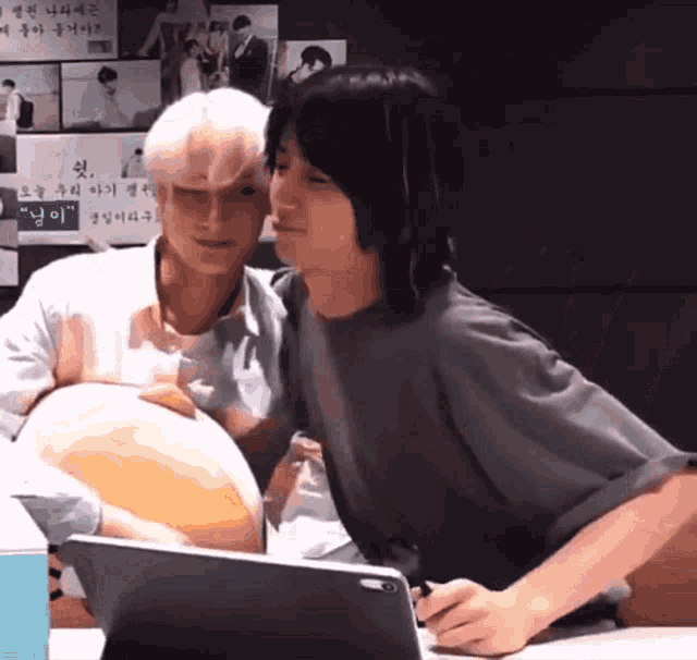 two young men are looking at a tablet and one of them is holding a large ball
