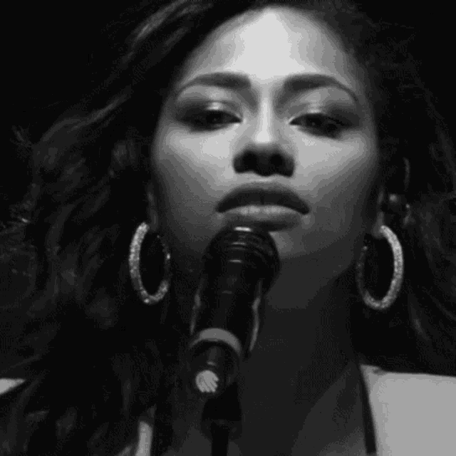 a woman singing into a microphone with hoop earrings on