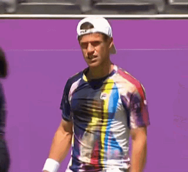 a man wearing a fila shirt and a white hat stands on a tennis court