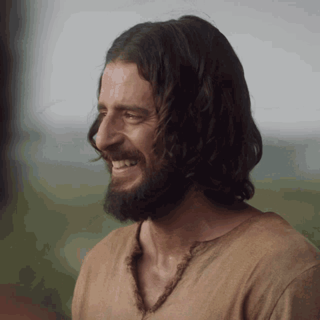 a man with long hair and a beard smiles in a field