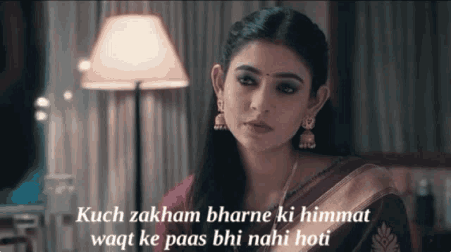 a woman in a purple saree is sitting in front of a lamp with the words kuch zakham bhare ki himmat