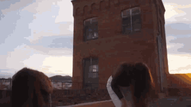 two women are standing on a rooftop looking at a brick building .