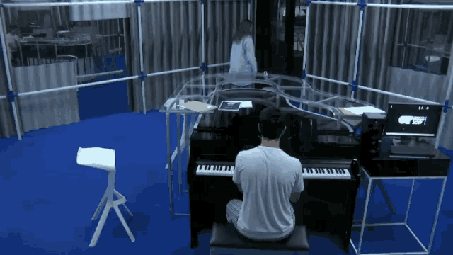 a man is playing a piano in a room with a computer screen that says ' new balance '