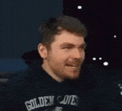 a man with a beard is wearing a black hoodie and laughing with his mouth open .