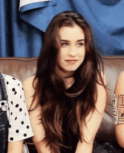 a woman with long brown hair is sitting on a couch and looking at the camera .