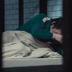 a man in a green shirt is laying on a bed with his head in his hands