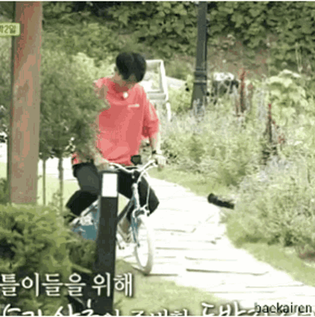 a man in a red shirt is riding a bicycle down a path