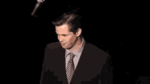 a man in a suit and tie is standing in the dark .
