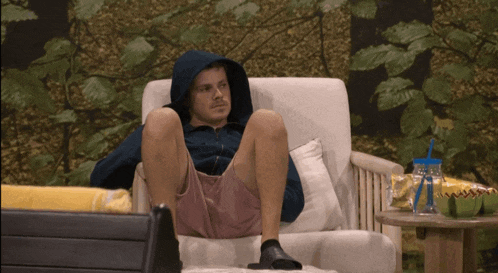 a man in a hooded jacket sits in a chair with his legs crossed