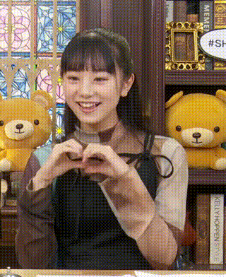 a girl is making a heart with her hands in front of a teddy bear