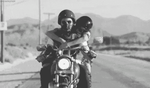 a man and a woman are riding a motorcycle down a desert road .